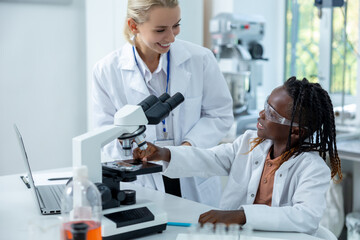Blonde teacher in white lab explaining how to work with microscope to a student