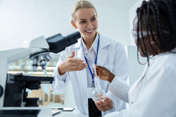 Fototapeta premium Blonde woman in lab coat explaining to a student how to sue microscope