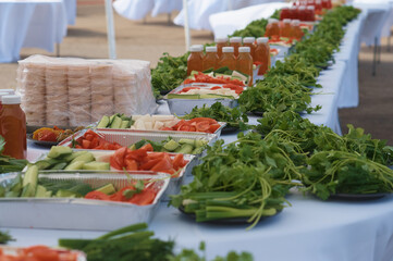 Large table with food outdoors. Close view of vegetables and greens. Healthy food at a corporate party. Selective focus. Healthy eating concept.
