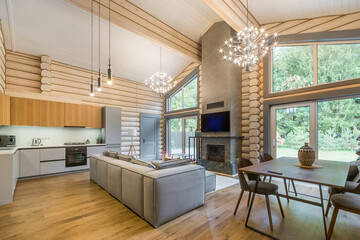 The interior of a living room with a fireplace in a luxurious log house with panoramic .windows. A picturesque summer landscape outside the window.