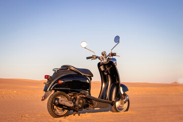 The Retro black scooter at sunset in the golden sand of the Namib Desert