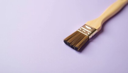 A paintbrush with a wooden handle and bristles, lying flat on a soft lilac background.