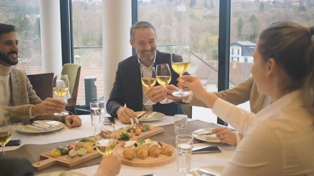 Smiling coworkers in restaurant toasting with wine during business lunch.