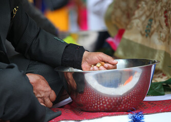 Man dropping nuts into a metal bowl during an Indian wedding ceremony