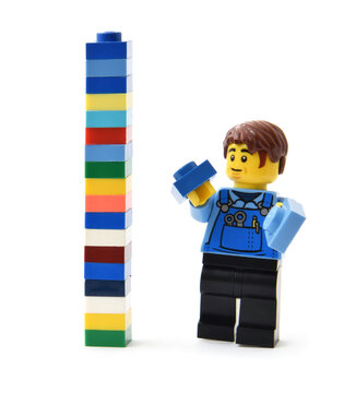 Lego minifigure is building a tall brick tower from colorful blocks. Editorial illustrative image of popular plastic toy constructor.