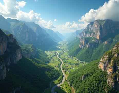 Aerial view of majestic mountain valley with winding road cutting through green landscape. Serpentine road meanders through rich valley. Rocky mountain peaks depth. Beautiful sky, clouds, sunlight
