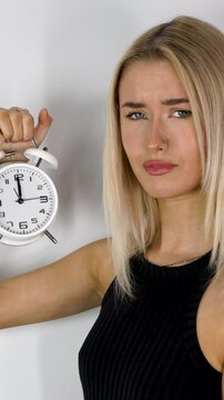 Portrait vertical footage of an attractive blonde haired woman holding up an old style alarm clock that is set to 12 o'clock, waking up at 12am or 12pm concept