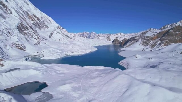 Ascending aerial drone view panorama of Tilicho Lake in Nepal, Annapurna Circuit trekking route. Clear blue glacial lake is surrounded by snowy mountains ranges during sunny day with clear blue sky