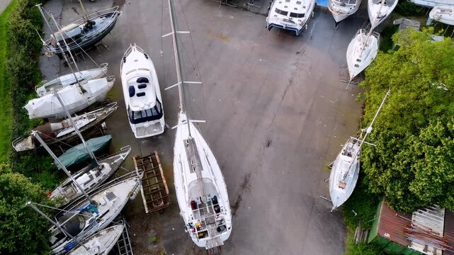 Antwerp Yacht Storage: Overcast Day Aerial View of Boats on Hardstanding - Assorted Sailboats and Catamarans, Grey Concrete, White Hulls, Green Vegetation, High Angle Drone Shot