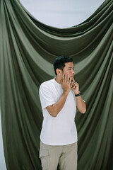 Thoughtful young man in contemplation with a draped green backdrop