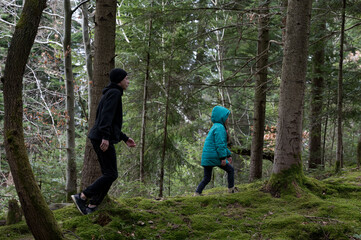 Fototapeta premium Two children exploring lush green forest terrain during a cool, overcast day filled with the tranquility of nature's harmony and the joy of discovery