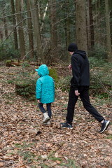 Fototapeta premium Enjoying a tranquil stroll through a lush forest during a cool afternoon, a parent and child share a moment of exploration and connection in nature's embrace