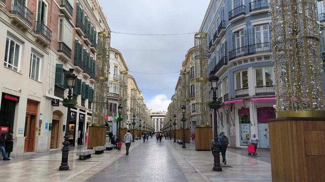 09.02.2025 Street in Malaga, Spain. Visitors leisurely stroll along a bustling street lined with festive decorations and shops.  Touristic place in Malaga. View from moving camera. 