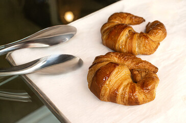 Freshly baked vegan croissants on a tray with tongs in a bakery