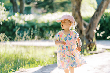 Little girl runs with her mouth open along a path in the park