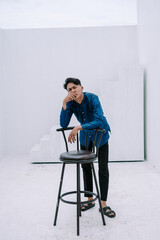 Contemplative young man resting on a stool in minimalist white studio