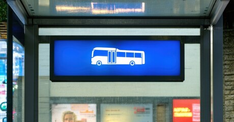 Vibrant blue rectangular bus stop sign white icon glowing softly lamppost casting reflections glass shelters neon ads