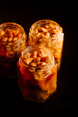 Homemade peanut butter jars filled with roasted peanuts, set against a dark background with a warm...
