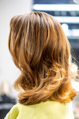 Naklejka premium Hair treatments at the hairdressing salon. Female hairdresser's hands brushing and blow drying blonde hair in beauty salon. Hairdresser cutting client's hair with scissors in salon
