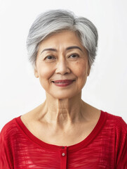 A smiling elderly woman with short gray hair wearing a red top against a plain background.