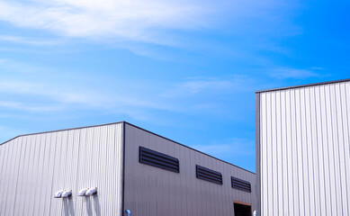 Obraz premium Two white factory industrial buildings structure with ventilation duct and louvers on aluminium corrugated metal wall in construction site against blue sky background, low angle view with copy space