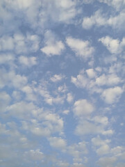 A serene sky filled with soft, scattered white clouds against a clear blue background, creating a peaceful and dreamy atmosphere.