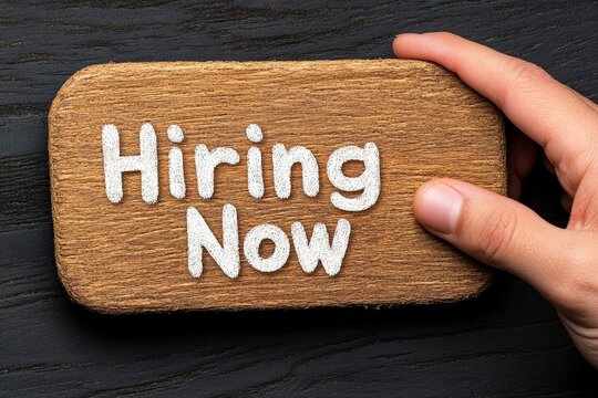 Hand Holding Wooden Sign with Text Hiring Now on Dark Background