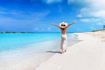 A happy woman with a sunhat walks down a tropical paradise beach in the Caribbean islands, Bahamas