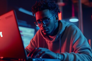 Young african male hacker focused on laptop in dark room with neon lights