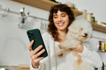 Young woman enjoys a joyful moment with her pet dog while checking her phone in the cozy kitchen