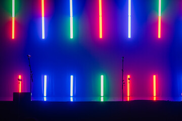 A stage with colorful LED lights in red, blue, and green, with microphone stands ready for a...