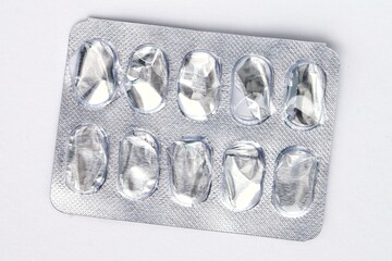 An empty blister pack is against a white background. The pack is made of silver foil with ten clear plastic compartments. The compartments are empty, showing their formed shape and transparency
