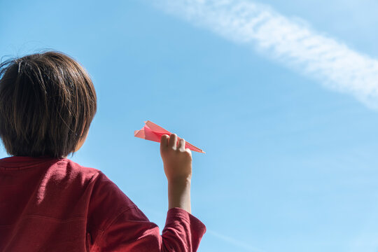 紙飛行機を手に持って空を見上げる子供と飛行機雲