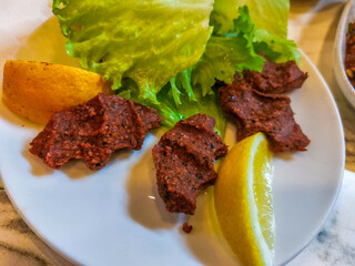Lettuce, lemon and raw meatballs (cig kofte) on a white plate. Traditional Turkish cuisine flavors. Top view.