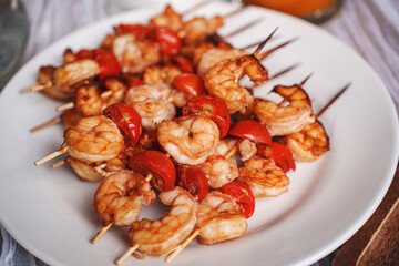 Skewers with shrimps and tomatoes on a white plate. 