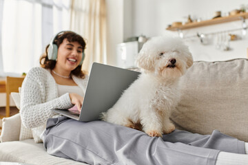 Young woman enjoying a cozy afternoon with her fluffy dog while working on a laptop at home