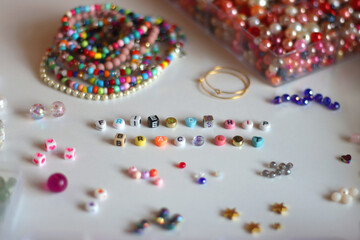 Friendship bracelet spelled with letter beads. Colorful handmade bracelets and various jewelry making supplies. Selective focus, white background.