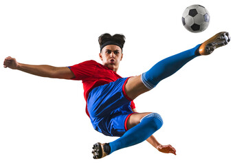 Portrait of young football player kicking ball in jump. Sportsman wearing red and blue uniform...