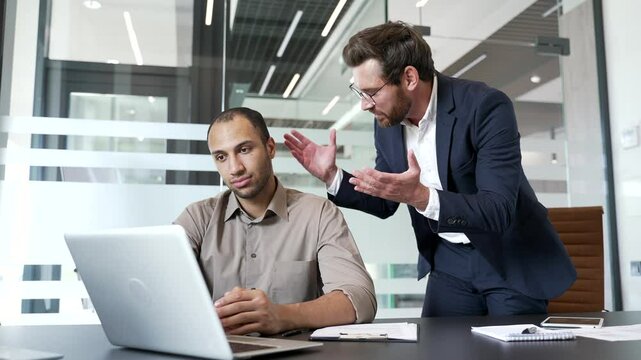 Angry mature boss quarreling with young male subordinate while sitting at workplace in business office. Furious executive arguing talking about problems. Dissatisfied manager unhappy with work results