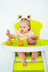 baby eats fruit puree in a high chair, baby food concept, little baby girl eats fruit on a white isolated background, place for text