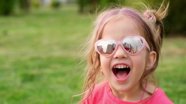 a child girl on a green lawn, a happy little child in glasses and a red T-shirt in summer on the grass rejoices and laughs, a place for text
