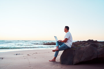 Freelancer working on laptop at beach during sunset enjoying freedom and remote work