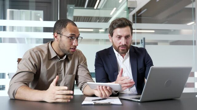 Two excited happy businessmen watching online results or cheering for bids at auction using laptop sitting in business office. Joyful colleagues celebrating success showing excitement and achievement