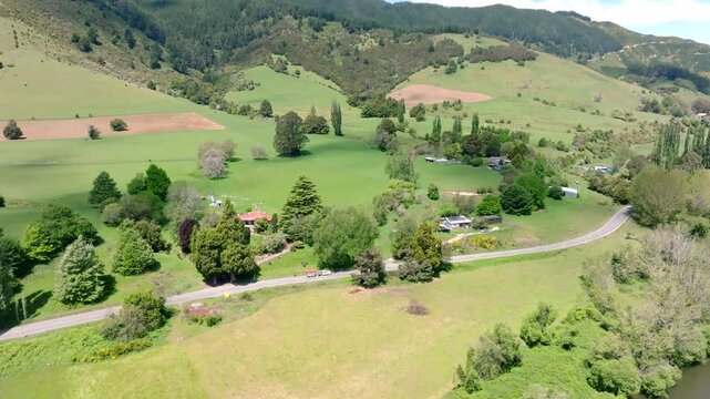 Aerial drone shot following a ute towing a boat along a winding country road beside the Motueka River in New Zealand on a sunny day.