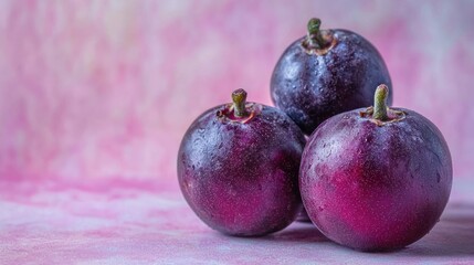 Three ripe, dark purple plums on pink background.