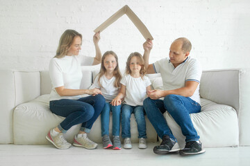 Happy family with children holding cardboard roof indoor. New house, real estate and insurance concept