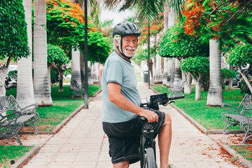 Happy active bearded senior man cycling in the public park with electric bicycle looking back at...