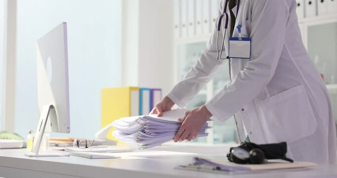 Brunette physician puts stack of medical records and sits down at desk. Woman doctor busy with systematic paperwork in healthcare office slow motion