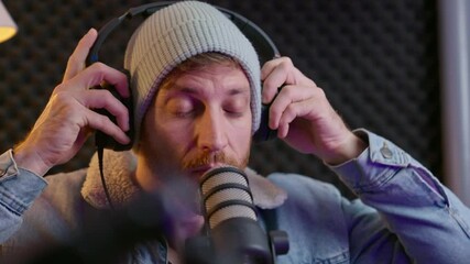 Man setting up professional audio gear in sound studio. Hipster male with beanie hat getting ready to record live streaming of radio voice over or podcast show. Using microphone and headphones indoors