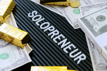 Business concept. Gold bars and dollars on a black background with the word solopreneur.